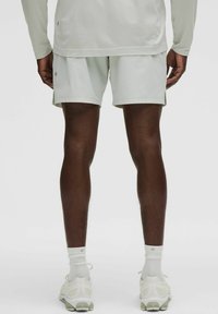 Helle graue Sportshorts und ein langärmliges Oberteil aus strukturiertem Stoff. Die Schuhe sind weiß mit grünen Akzenten und werden mit weißen Socken kombiniert.