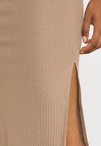 Robe midi en maille couleur beige clair avec des côtes verticales, dotée d'une fente latérale et d'une texture lisse. Design simple sans éléments métalliques visibles.
