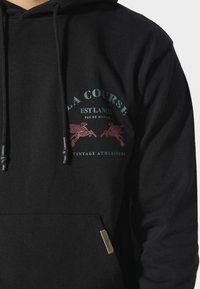 Sudadera negra de mezcla de algodón, con un bolsillo tipo canguro en la parte delantera, capucha con cordón y un diseño impreso con dos caballos alados.