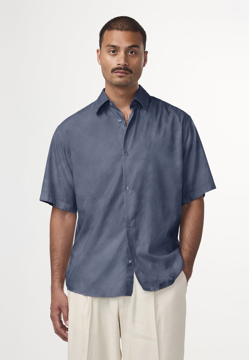 Chemise à manches courtes avec boutons de couleur bleu marine, fabriquée en tissu lisse. Dotée d'un col classique et d'une coupe décontractée, elle est complétée par un ourlet droit.