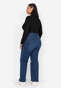 Högmidjade blå denimjeans med avslappnad passform, med bakfickor och en lätt textur, kombinerade med en långärmad svart topp.