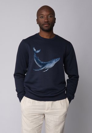 Marine sweatshirt met een grote, gedetailleerde walvisafbeelding in blauw tinten. Ribgebreide boorden en een ronde hals, gecombineerd met lichte broeken.