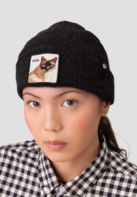 Beanie nero in maglia con un'etichetta quadrata raffigurante un'immagine di un gatto siamese e la parola "COOL" ricamata sopra.