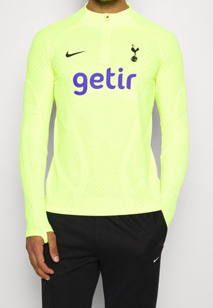 Homme portant un haut d'entraînement Tottenham Hotspur à manches longues de couleur jaune fluo avec le logo violet "getir" et un pantalon de survêtement Nike noir.