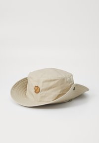 Chapeau seau beige en tissu léger, doté d'une large bordure et d'un patch logo cousu avec un motif de renard sur le devant.