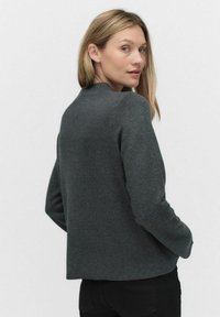 Hiilenharmaa neulepaita, joka on valmistettu pehmeästä neulemateriaalista. Sosiaalisina ominaisuuksina on pyöreä pääntie, pitkät hihat ja suora helma. Minimalistinen muotoilu.