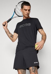 Crna sportska majica s "BORG" logotipom, u kombinaciji s odgovarajućim kratkim hlačama. Majica ima kratke rukave i ležeran kroj.