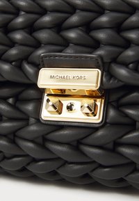 Schwarze Lederhandtasche mit geflochtenem Design, ausgestattet mit einem goldenen Metallverschluss und einem "MICHAEL KORS"-Logo-Schild. Strukturierte Oberfläche, geometrische Form.