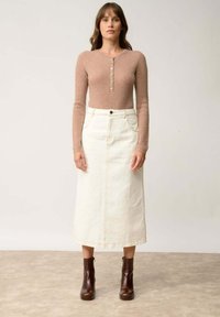 Rybkowany, jasnobrązowy, długi rękaw z detalem guzika, w połączeniu z białą, dżinsową spódnicą midi. Ciemnobrązowe botki za kostkę dopełniają stylizację.