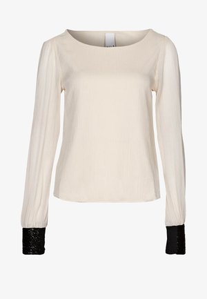 Blouse crème à manches longues en tissu texturé avec poignets en sequins noirs contrastants, dotée d'un col rond et d'une coupe décontractée.