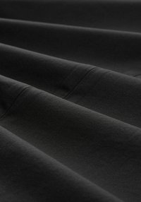 Czarna tkanina o gładkiej fakturze, z widocznymi miękkimi fałdami. Materiał wydaje się elastyczny i lekki, co sugeruje wygodę i wszechstronność.