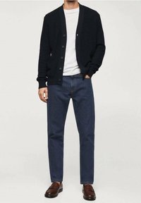 Cárdigan de punto azul marino con escote en V y botones en la parte delantera, combinado con una camiseta blanca de cuello redondo y jeans de mezclilla oscuros, complementado con mocasines marrones.