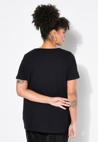 Camiseta negra de manga corta con un corte relajado y un escote redondo, que presenta una textura suave y un diseño liso, combinada con pantalones negros.