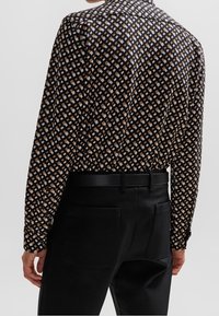 Langarm-shirt in een zwarte stof met een geometrisch patroon van bruine en lichtblauwe vierkanten, gecombineerd met een zwarte broek en een zwarte riem.