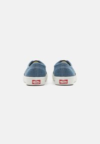 Scarpe slip-on in denim blu con suole in gomma bianca e un caratteristico logo rosso sul tallone, dotate di dettagli di cucitura lungo i bordi.