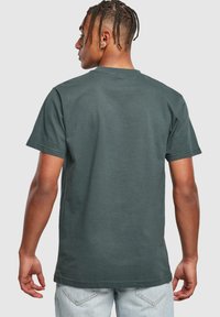 Mørkegrøn bomulds T-shirt med korte ærmer, rund hals og en glat tekstur, vist fra ryggen mod en ensfarvet baggrund.