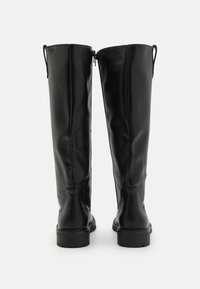 Bottes noires montantes en cuir lisse, avec un design épuré, des zips latéraux et une semelle épaisse et texturée.