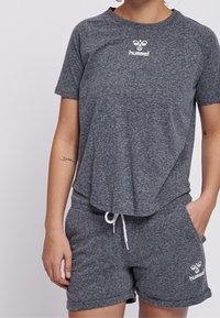Šedý sportovní set trička a šortek vyrobený z texturované látky. Tričko má logo na hrudi a šortky mají šňůrku v pase a boční kapsy.