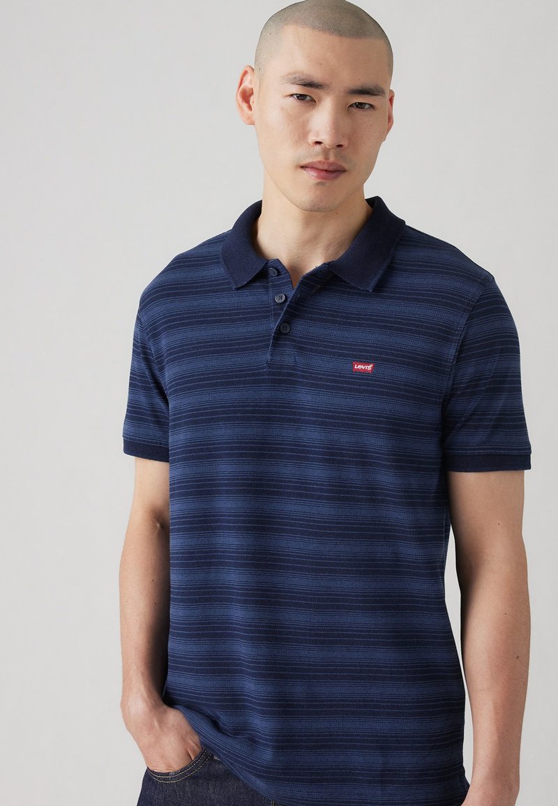 Polo de culoare albastru marin cu dungi, confecționat din bumbac, având un guler clasic, placket cu trei nasturi și un mic logo Levi's roșu pe piept.