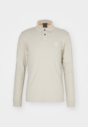 Long-sleeve polo shirt in light beige cotton. Features a collar, two buttons, and a small, embossed logo on the chest. Orange inner collar.