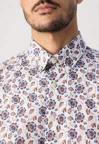 Λευκό πουκάμισο με φλοράλ σχέδιο σε μπλε και πορτοκαλί αποχρώσεις, με γιακά που κουμπώνει και μπεζ κουμπιά. Απαλή υφή υφάσματος.