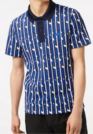 Niebieska i biała koszulka polo w wzory, z granatowym kołnierzykiem, ozdobiona geometrycznymi wzorami oraz małym niebieskim logo na piersi.