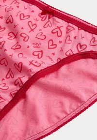 Roze katoenen slipjes met een herhaald hartpatroon in donkerdere schakeringen van roze, met een delicate rode rand en een kleine strikaccent.
