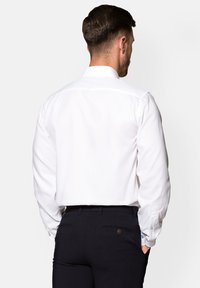 Biała koszula z długimi rękawami, z klasycznym kołnierzykiem i gładką fakturą, w połączeniu z ciemnymi spodniami z delikatnym przeszyciem.