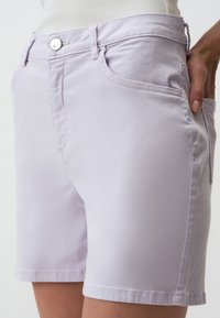 Shorts lavande clair en tissu mélangé coton, dotés d'un bouton argenté unique, de poches avant et de détails de couture à l'ourlet.