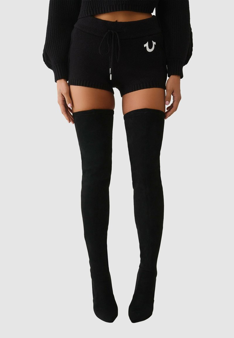 Czarne dzianinowe spodenki z prążkowanymi brzegami i ściągaczem w pasie, zestawione z wysokimi czarnymi zamszowymi kozakami sięgającymi ud. Charakterystyczne metalowe detale na spodenkach.