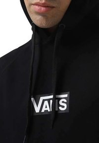 Sudadera negra con un bolsillo canguro en la parte frontal, que presenta un logo blanco de "VANS". Tejido suave con capucha ajustable y puños acanalados.