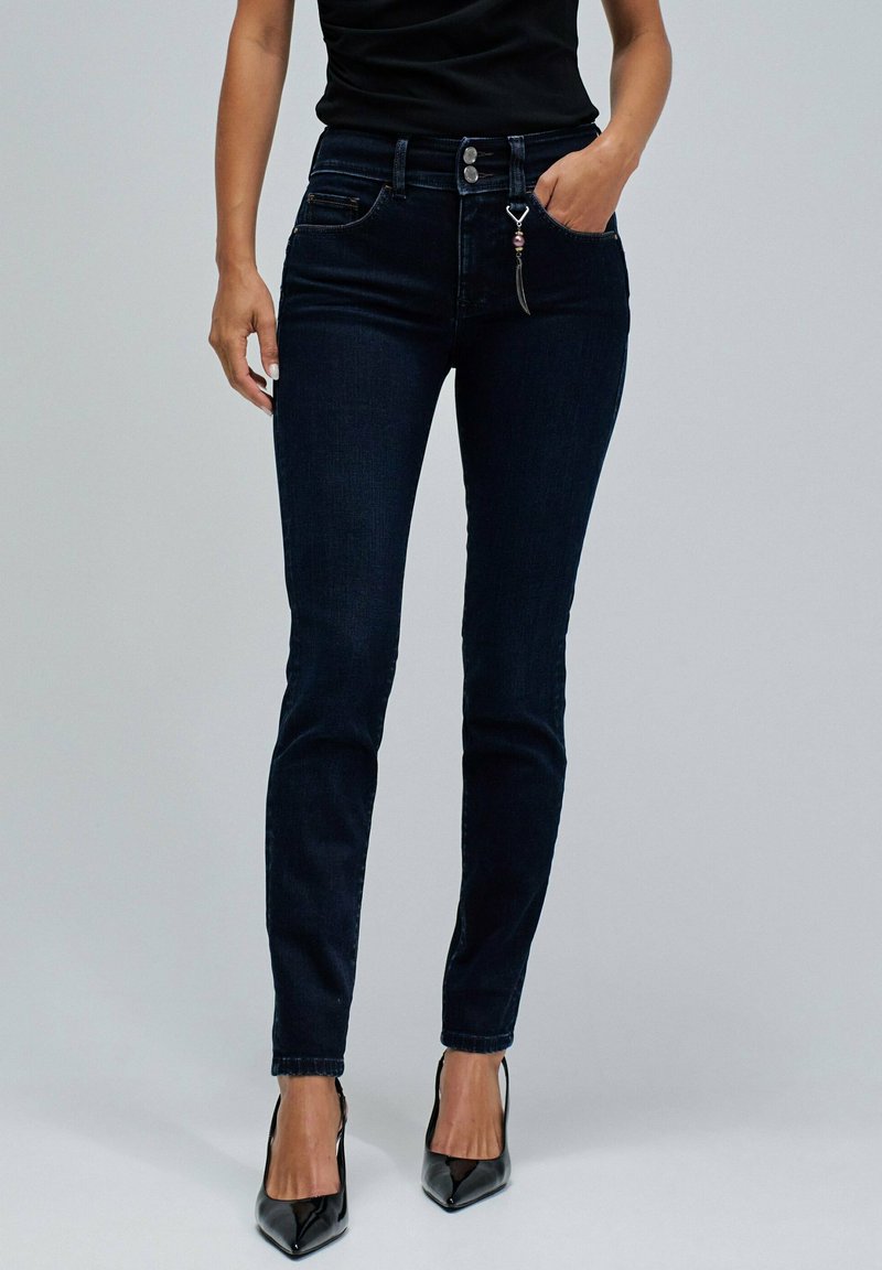 Jeans ajustados de color azul oscuro hechos de mezclilla, con una cintura alta, bolsillos frontales y un detalle de cremallera metálica con un charm decorativo.