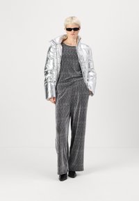 Doudoune argentée, combinaison texturée grise, lunettes de soleil noires et bottines. La tenue présente une finition brillante et une coupe loose.