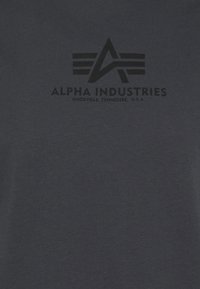 Tmavě modré tričko vyrobené z bavlny, s černěti potisknutým logem s křídly a textem "ALPHA INDUSTRIES, KNOXVILLE, TENNESSEE, U.S.A."