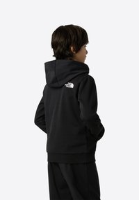 Fekete kapucnis pulóver puha anyagból, kenguruzsebbel, bordázott mandzsettákkal, és fehér The North Face logóval a háton.