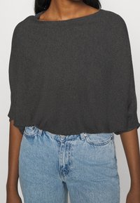 Dunkelgraues Strickoberteil mit weitem Ausschnitt und kurzen Ärmeln, kombiniert mit hellblauen, hochtaillierten Jeans aus Denim. Strukturiert. 