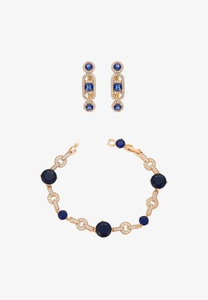 Złoty zestaw biżuterii z bransoletką ozdobioną granatowymi kamieniami i przezroczystymi kryształami oraz pasujące kolczyki o owalnych i okrągłych kształtach.