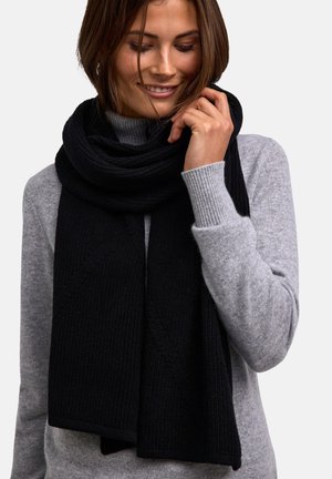 Scarf in maglia nera drappeggiata attorno al collo, con una texture a coste e motivi diagonali, contrastata da un maglione grigio.