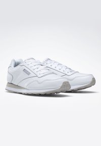 Weiße Sportschuhe mit glattem Lederobermaterial, Schnürdesign, gepolstertem Kragen und strukturiertem Gummiaußensohle. Dezentes Logo an der Seite.