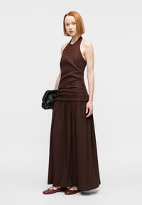 Καφέ τοπ με ράντες και εφαρμοστή μέση, συνδυασμένο με πλεκτή μάξι φούστα, ένα υφασμάτινο μαύρο τσαντάκι και κόκκινα επίπεδα παπούτσια. Ομαλή υφή υφάσματος.