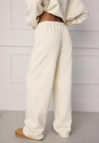 Cream-colored sweatpants made of soft fabric with an elastic waistband, featuring a relaxed fit and turned-up cuffs, paired with tan slippers.