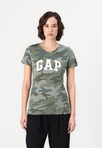 Grønn camo t-skjorte med rund hals, korte ermer og hvit "GAP"-logo på forsiden. Myk bomullsmateriale.