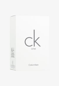 Scatola rettangolare bianca con testo grigio che mostra "ck one" e "Calvin Klein". Include etichette di cura e certificazione sui lati.