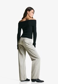 Svart ribbad off-shoulder topp i kombination med ljusgrå vida jeans och svarta spetsiga stövlar. Fokus ligger på den figurnära toppen och den avslappnade byxdelen.