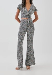 Ensemble deux pièces à imprimé floral composé d'un haut cache-cœur avec manches à volants et d'un pantalon évasé, en tissu foncé avec de petites fleurs pastel.