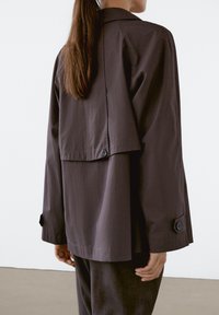 Dark gray, lightweight jacket with a cropped back, large collar, and buttoned cuffs. Features a smooth texture and loose-fitting design.