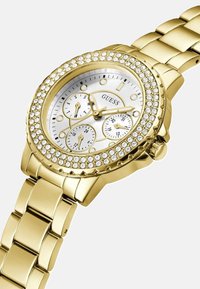 Kultainen ruostumattomasta teräksestä valmistettu kello, jossa on kristallikoristeinen kehä, hopeinen kellotaulu ja kolme pienempää näyttöä tyylikkäällä, linkkikiinnityksellä varustetulla hihnalla.