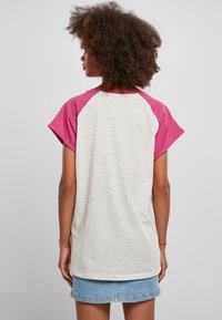 Grå og rosa raglan t-skjorte med korte ermer. Stoffet ser mykt ut, med en glatt tekstur. Designet har kontrastfargede ermer.
