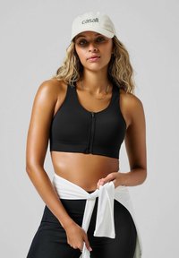 Czarny sportowy stanik na zamek z szerokimi ramiączkami i g�ładką teksturą, zestawiony z białym materiałem związanym w talii. Swobodne beżowe czapka z logo.
