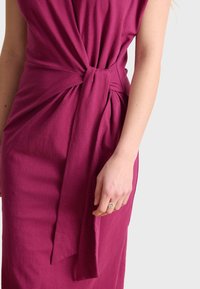 Fuchsia dress made of soft fabric, featuring a twisted knot detail at the waist and a sleek, form-fitting design.